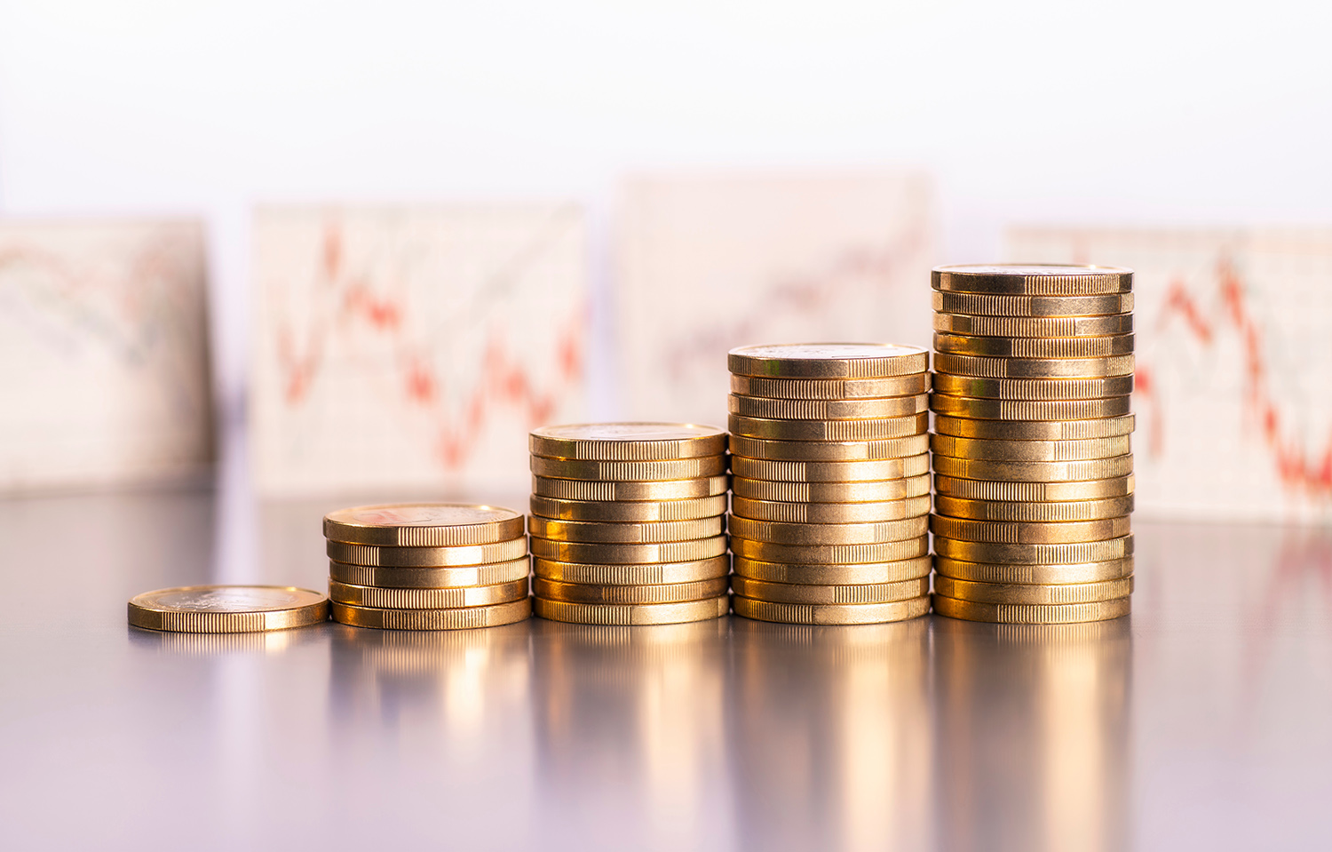 Ansteigende Stapel mit Münzen und Charts mit Aktienkursen im Hintergrund